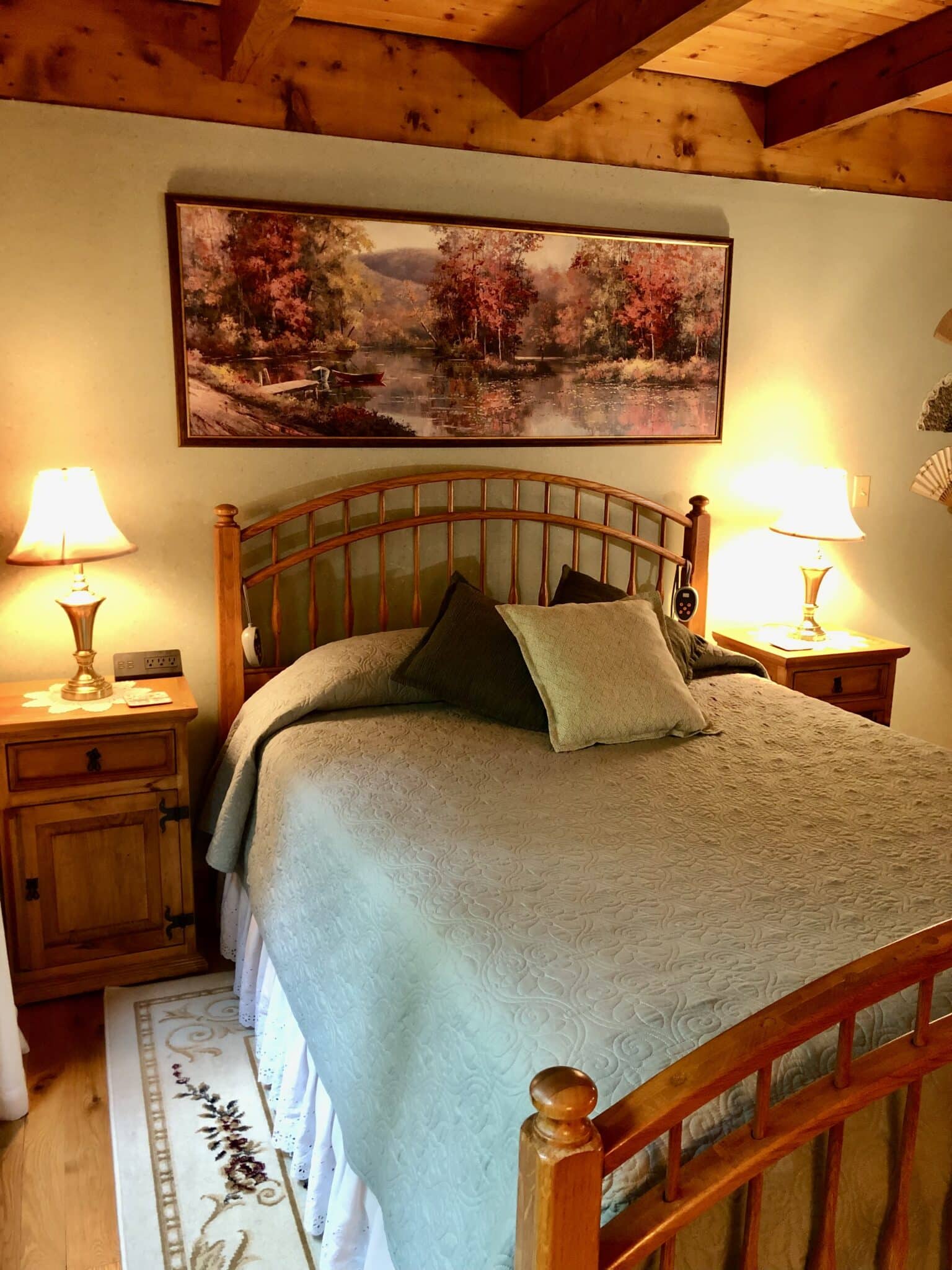 The Monument Room Queen size bed, 2 nightstands and lamps under a fall forest painting.