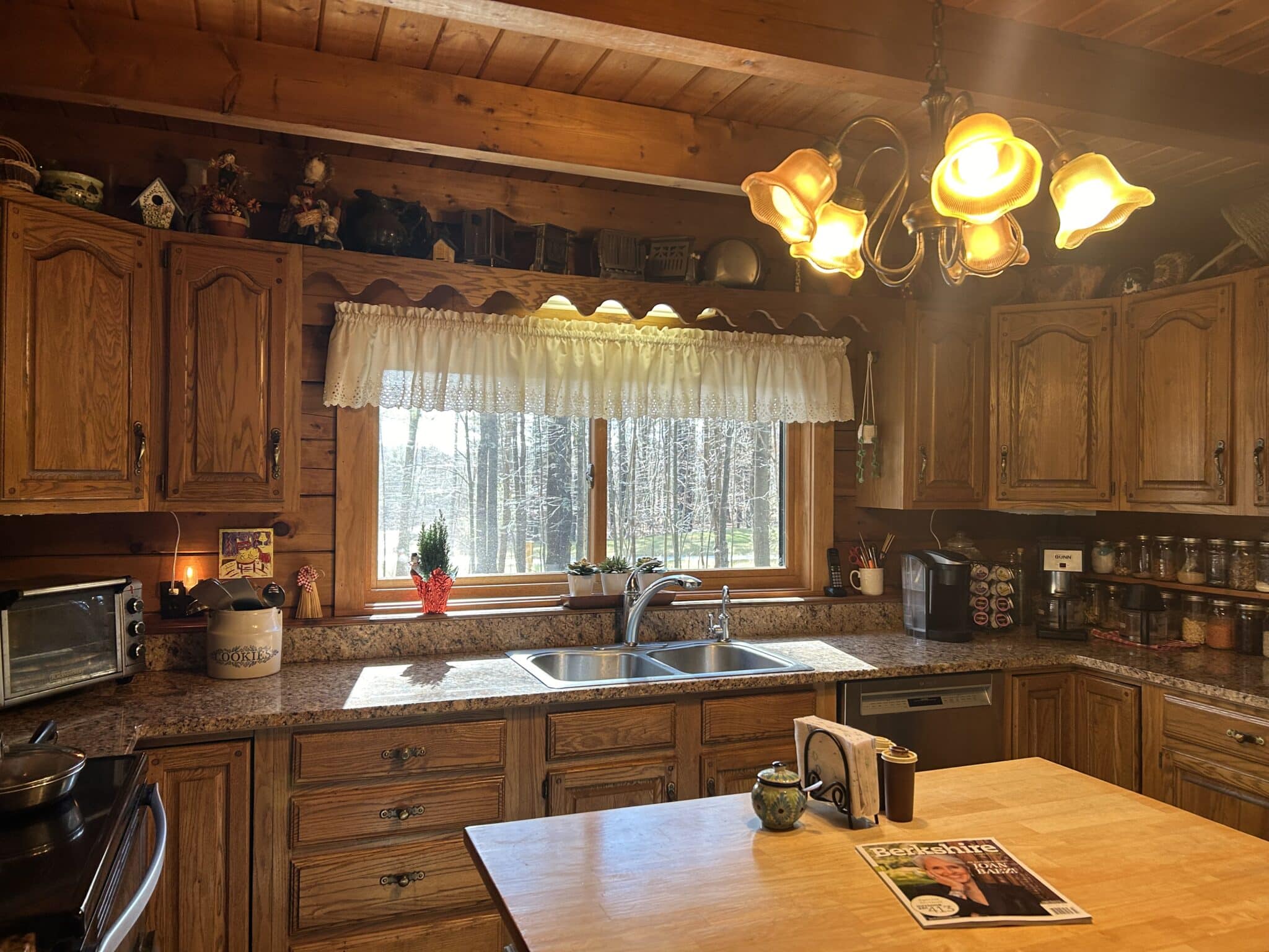 The kitchen has wood cabinets, butcherblock island and a view out the large window of the forest.