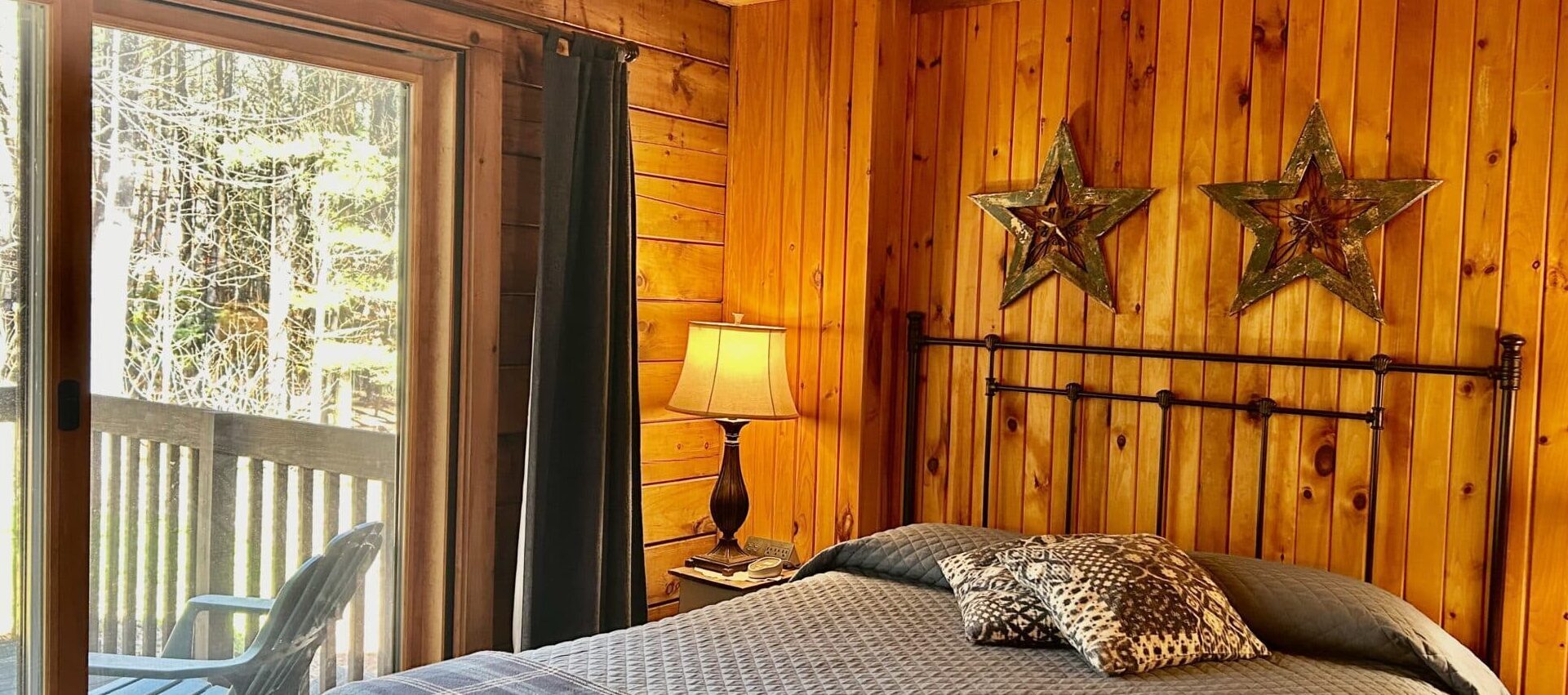 The Everett Room with Queen size bed and nightstand with lamp.  Looking out glass door into forest.