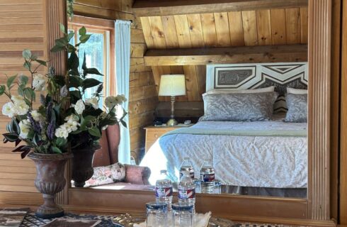 view of room through dresser mirror of bed and accessories on dresser, flowers on left.