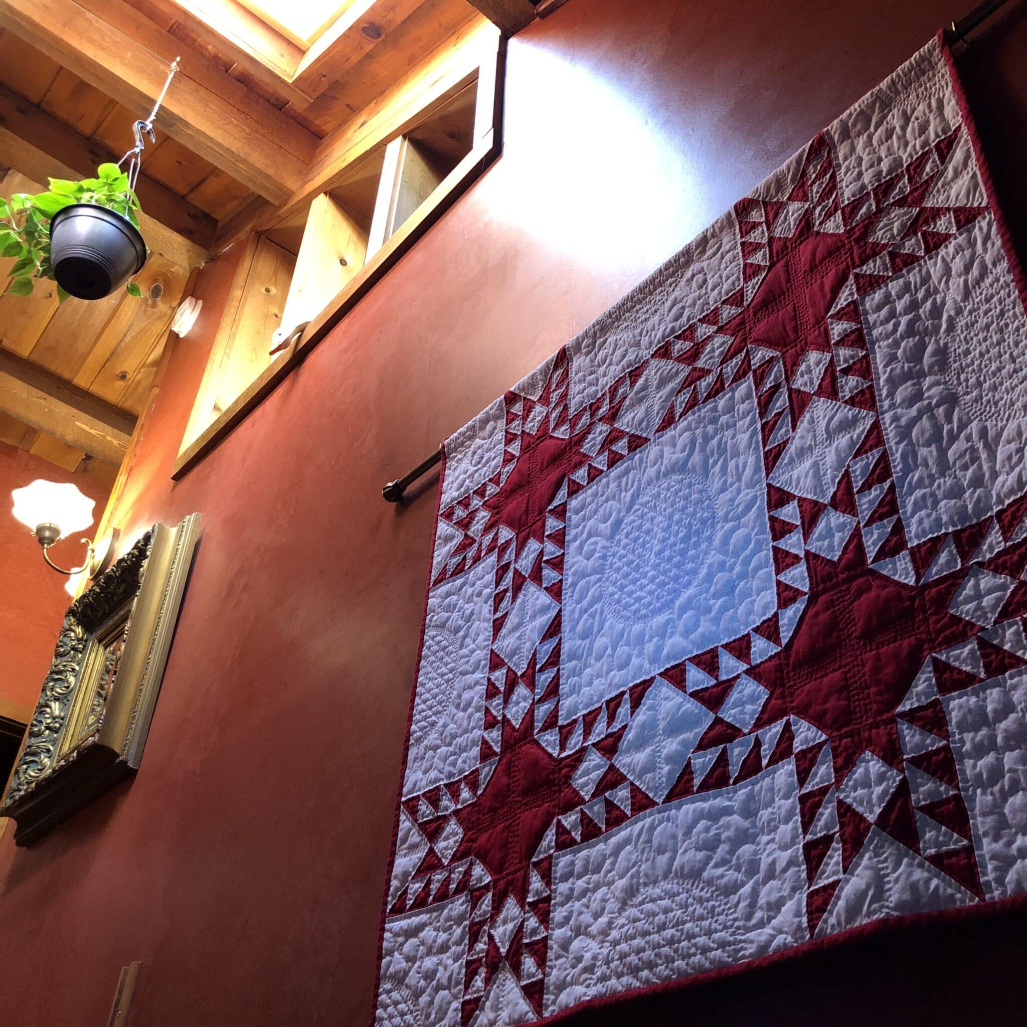 Hanging on the stairwell wall is an antique quilt sampler in red and white patchwork fabrics.