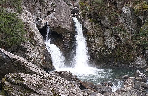 Two small waterfalls cascading out of rock and boulders into a pool below