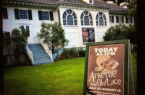 White theatre building with arched windows and advertising sign out on front lawn