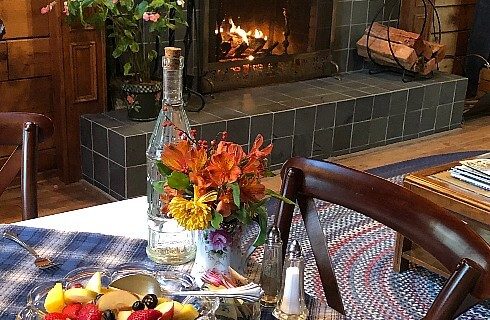 Dining table set for breakfast next to a lit fireplace with grey tile