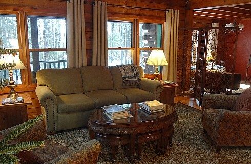 Living area of a home with couch, two sitting chairs and coffee table in front of four large windows with white curtains