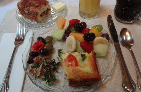 Round glass plate with slice of breakfast quiche and fruit salad with orange juice, coffee and slice of coffee cake