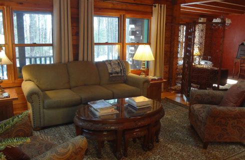 Couch with two sitting chairs in front of large windows with white curtains, next to a foyer area with table and decorative screen