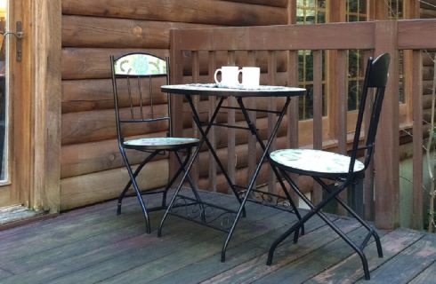 Small bistro table with two white cups, two chairs on an outdoor patio with wooden railing