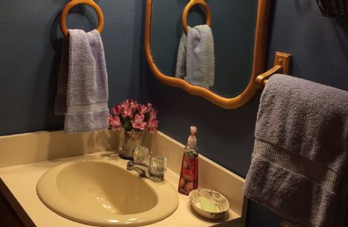 Single sink vanity with wood framed mirror in a bathroom with dark walls and towels hanging on wooden rods