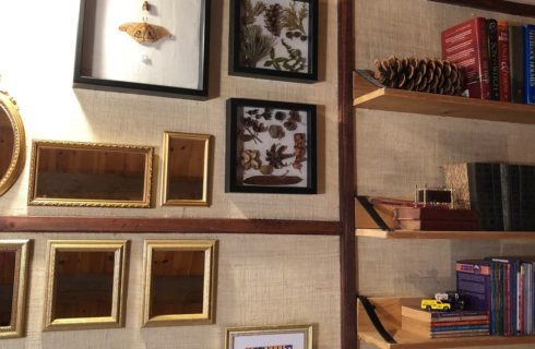 Gallery wall featuring gold framed mirrors, framed leaves and three wooden shelves with books