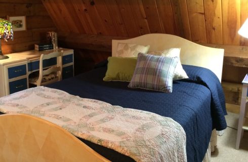 Double sized bed blue and white quilt and accent pillows next to writing desk with multi-colored Tiffany lamp