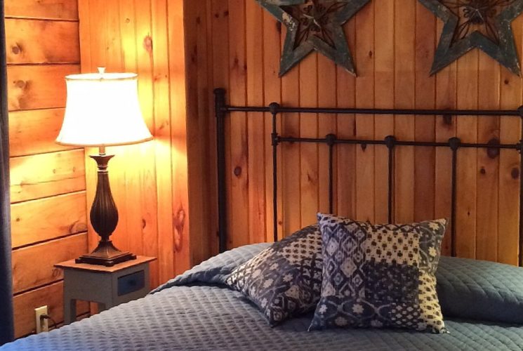 Queen bed with black wrought iron headboard and blue quilt, two side tables with lamps in a room with wood paneled walls