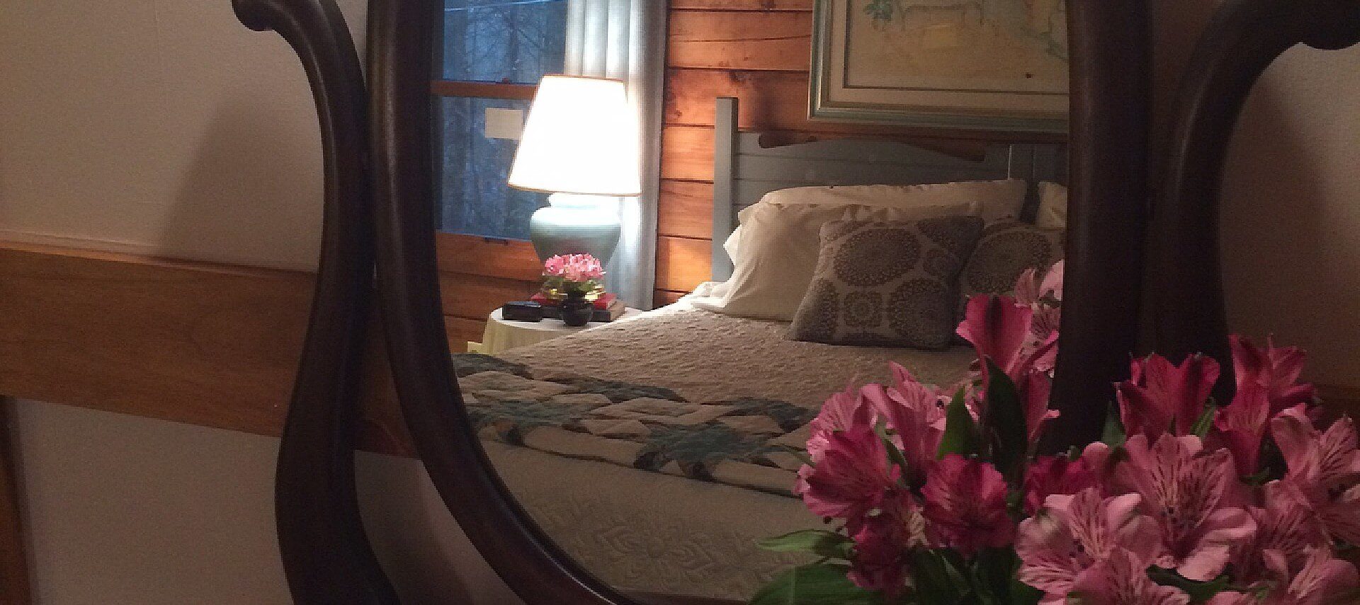 King bed with blue headboard and white quilt reflecting in a large oval antique mirror