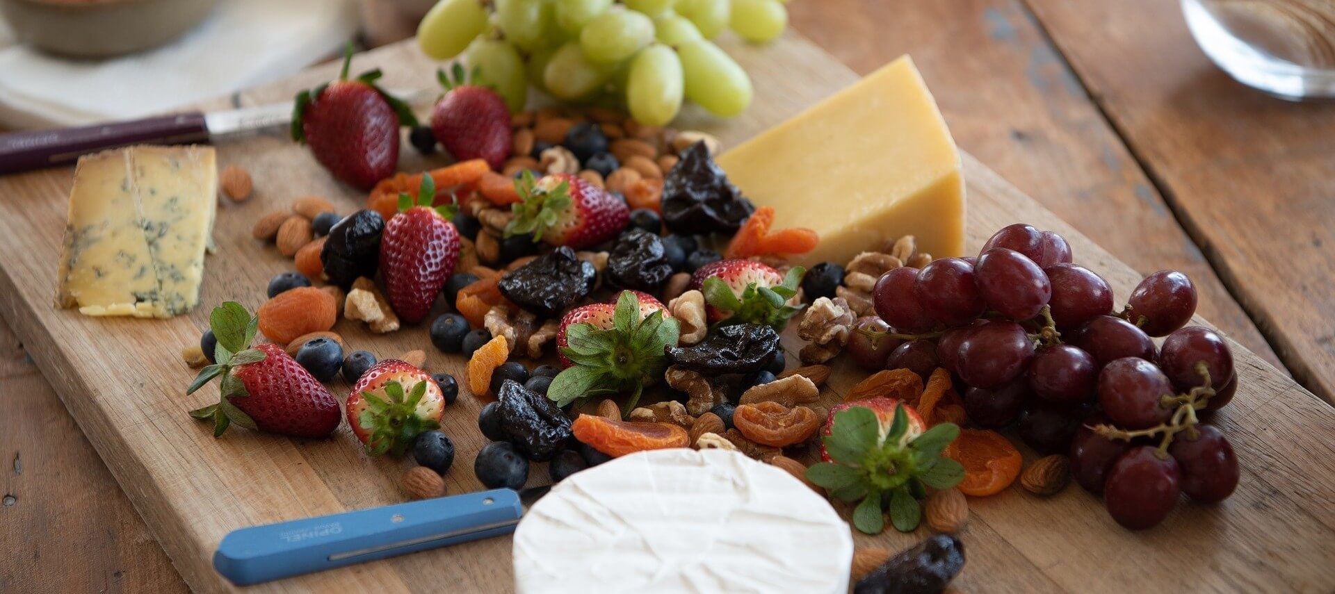 Cutting board full of fruit, nuts and wedges of three different types of cheese