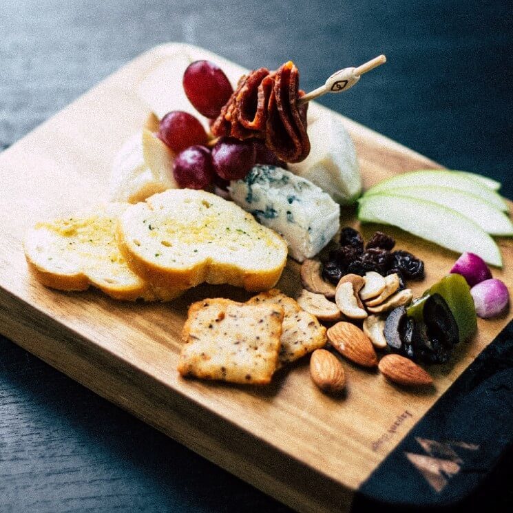 Charcuterie board with bread, crackers, nuts, apples, cheeses and skewer of grapes and meat