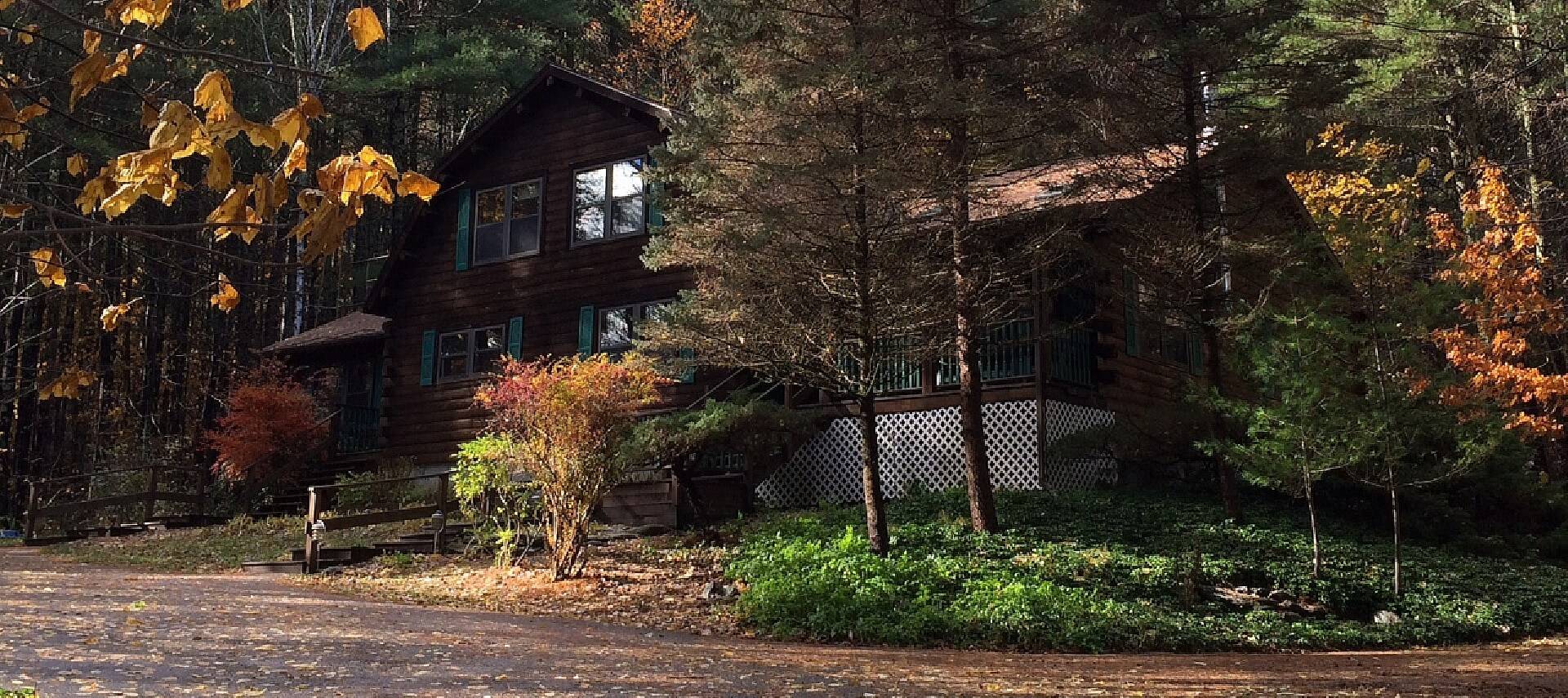 Large dark wood cabin home nestled in a wooded area with green shutters on the windows and stairway up to a front porch
