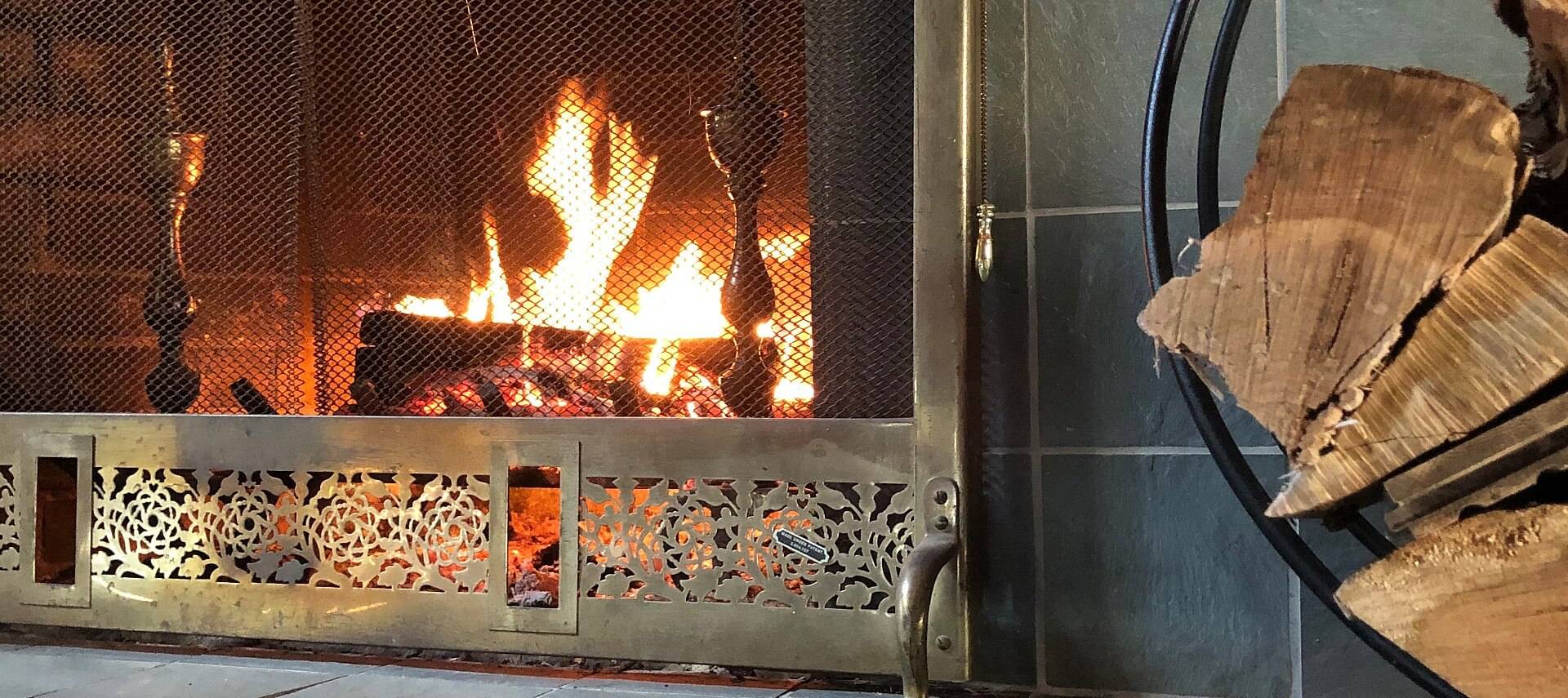 Roaring fire with logs in a grey tiled fireplace with decorative screen in front