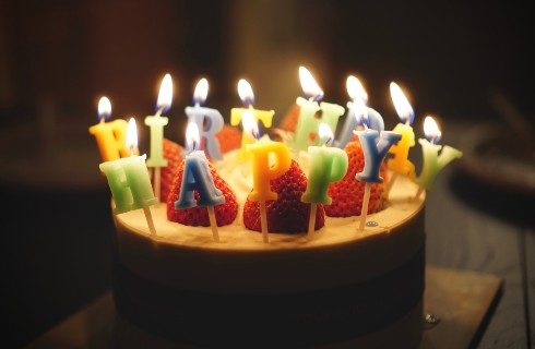 Round cake topped with strawberries and lit candles that spell out happy birthday